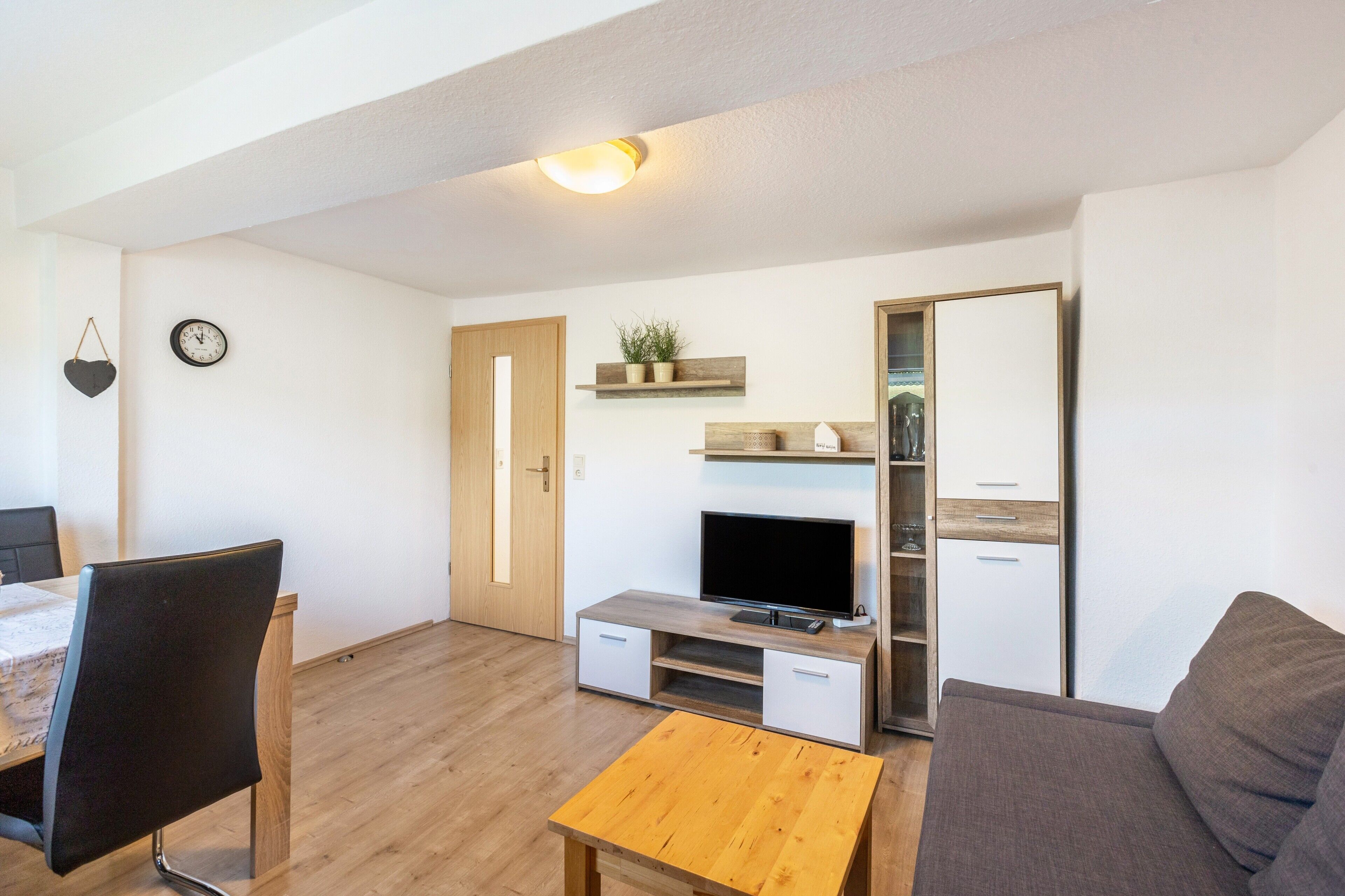 Een moderne woonkamer met een flatscreen televisie, een houten salontafel, een bank en een eethoek met een tafel en stoelen.