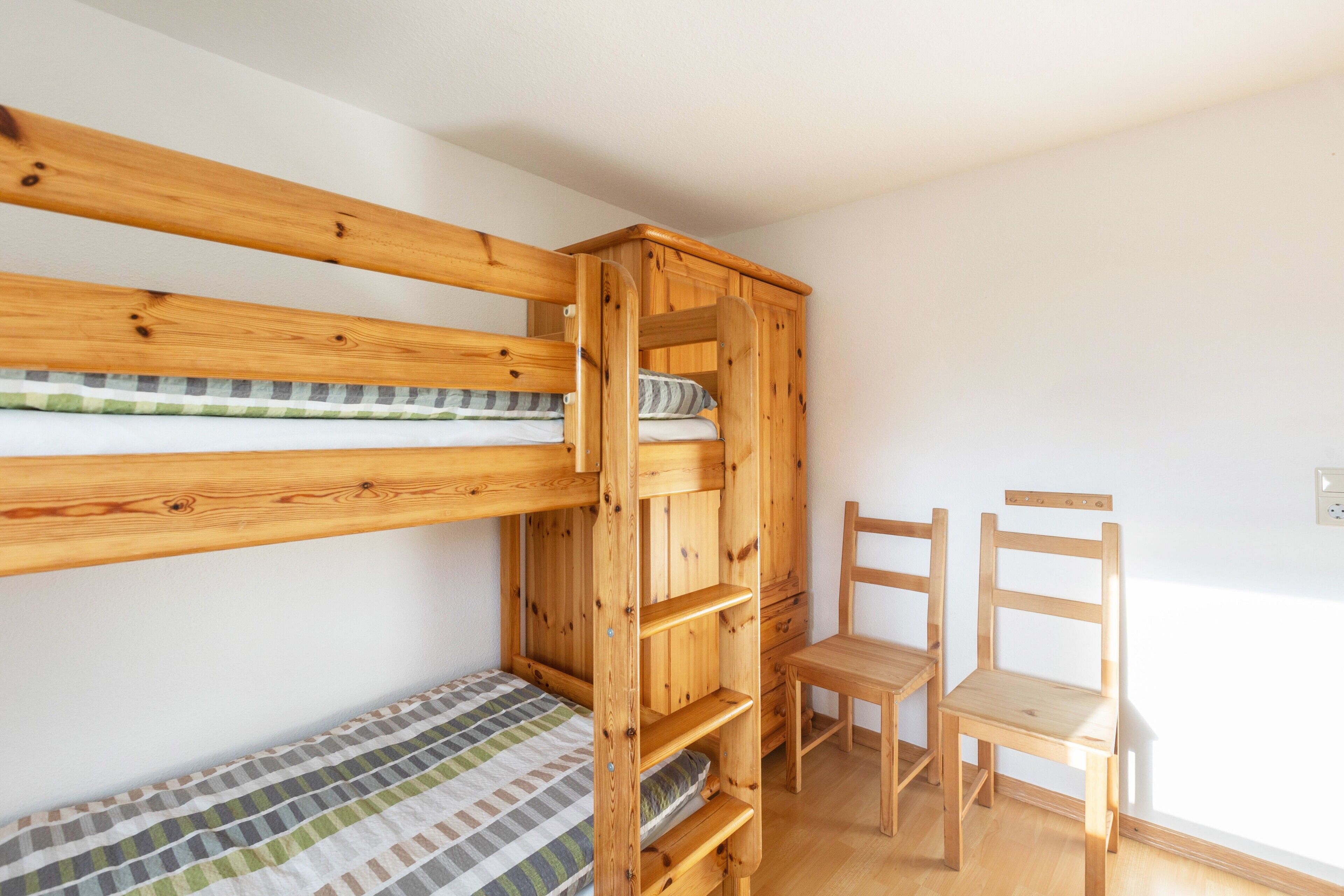 Un letto a castello con struttura in legno, un letto singolo in basso e due sedie di legno.