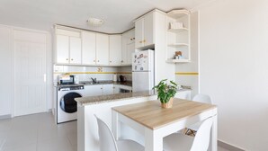 A modern kitchen with white cabinets, a built-in washing machine, a wooden dining table with chairs, and a small potted plant. - Apartment 'Bahía Mar' with Sea View, Private Terrace and Wi-Fi (Puerto de Mazarrón)