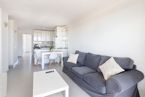 Un salon moderne avec un canapé gris, une table basse blanche et une cuisine en arrière-plan.