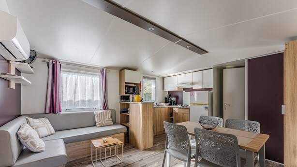 Un espacio habitable compacto con sofá, mesa de comedor, sillas, kitchenette y una ventana con cortinas.