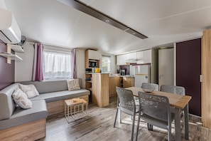A compact living space with a sofa, dining table, chairs, kitchenette, and a window with curtains.