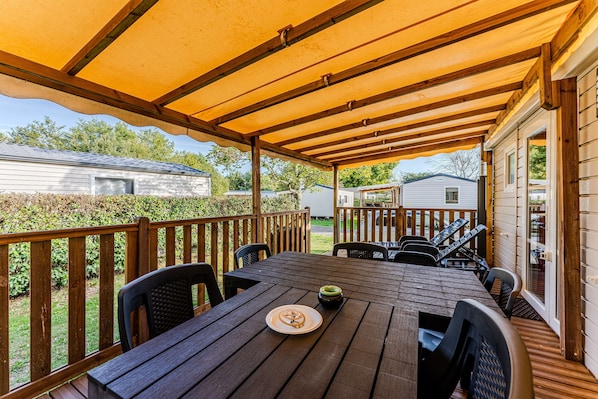 A covered patio with a wooden table and chairs, a small table with a plate and a bowl, and a view of neighboring houses.