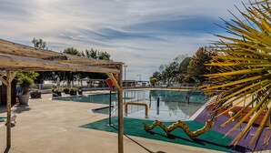 Un área de piscina con una pérgola de madera, un trampolín y una palmera.