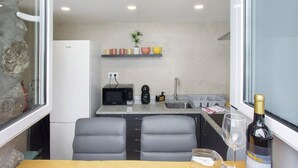 A compact kitchen with a microwave, sink, and a small shelf with cups.