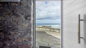 A stone wall, a door leading to a balcony with a view of the sea, and a modern door with a handle.