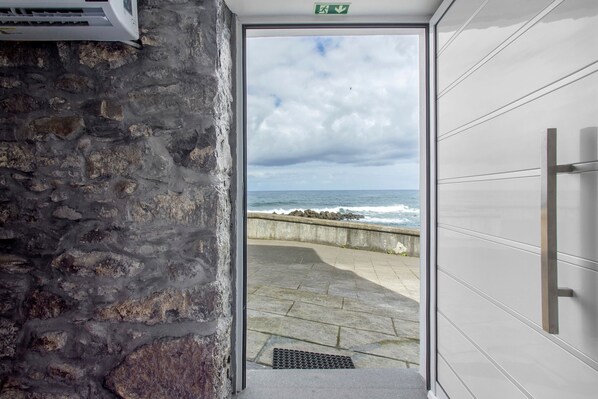 A stone wall, a door leading to a balcony with a view of the sea, and a modern door with a handle.