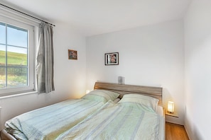 A bedroom with a bed, a window with curtains, a nightstand with a lamp, and two framed pictures on the wall. - Apartment 'Gänseblümchen' with Shared Terrace and Wi-Fi (Schmallenberg)