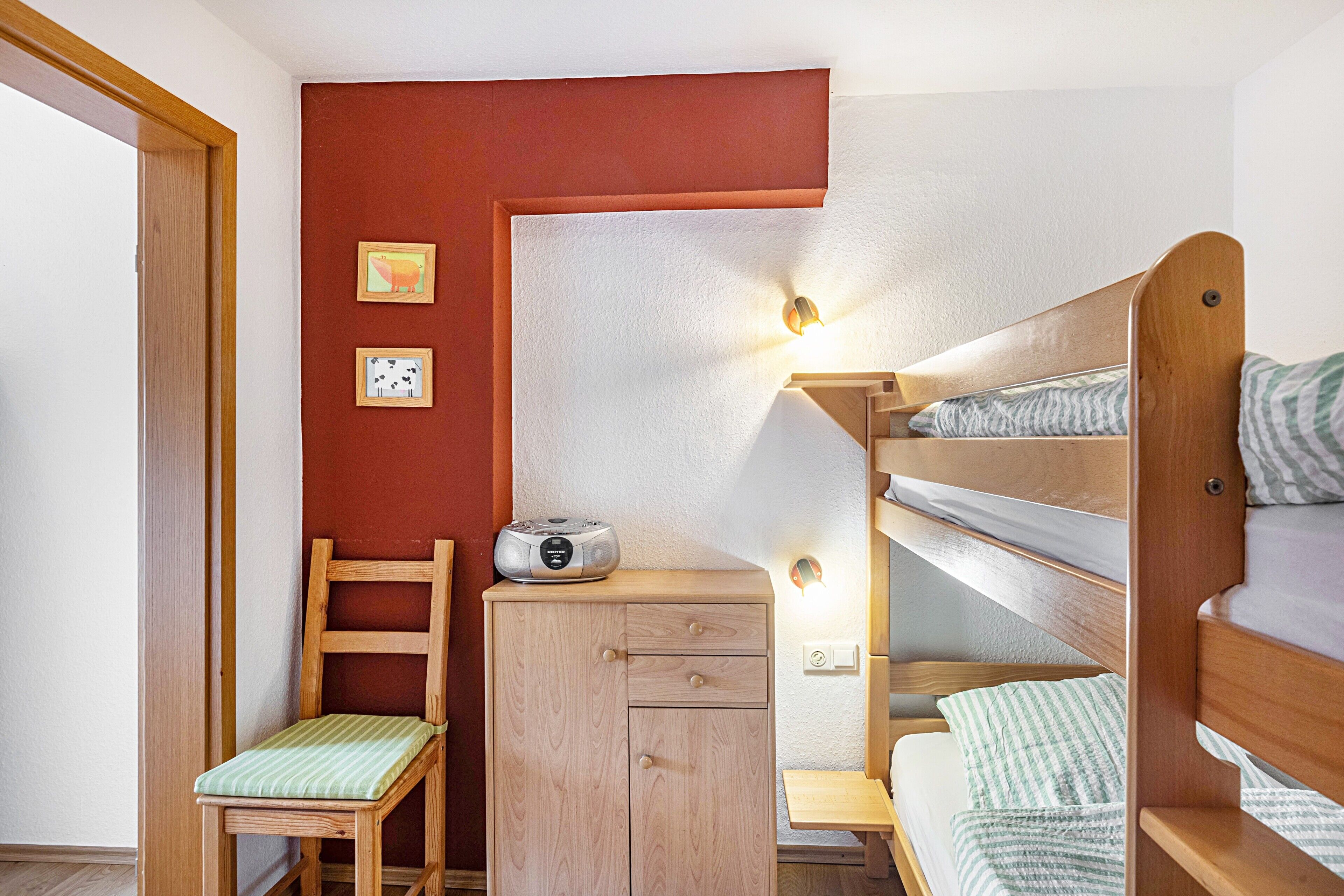 A bunk bed with a wooden headboard, a desk with a chair, and a small cabinet.