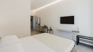 Een moderne hotelkamer met een bed, een bureau, een stoel, een aan de muur bevestigde televisie en een klein tafeltje met dienblad.