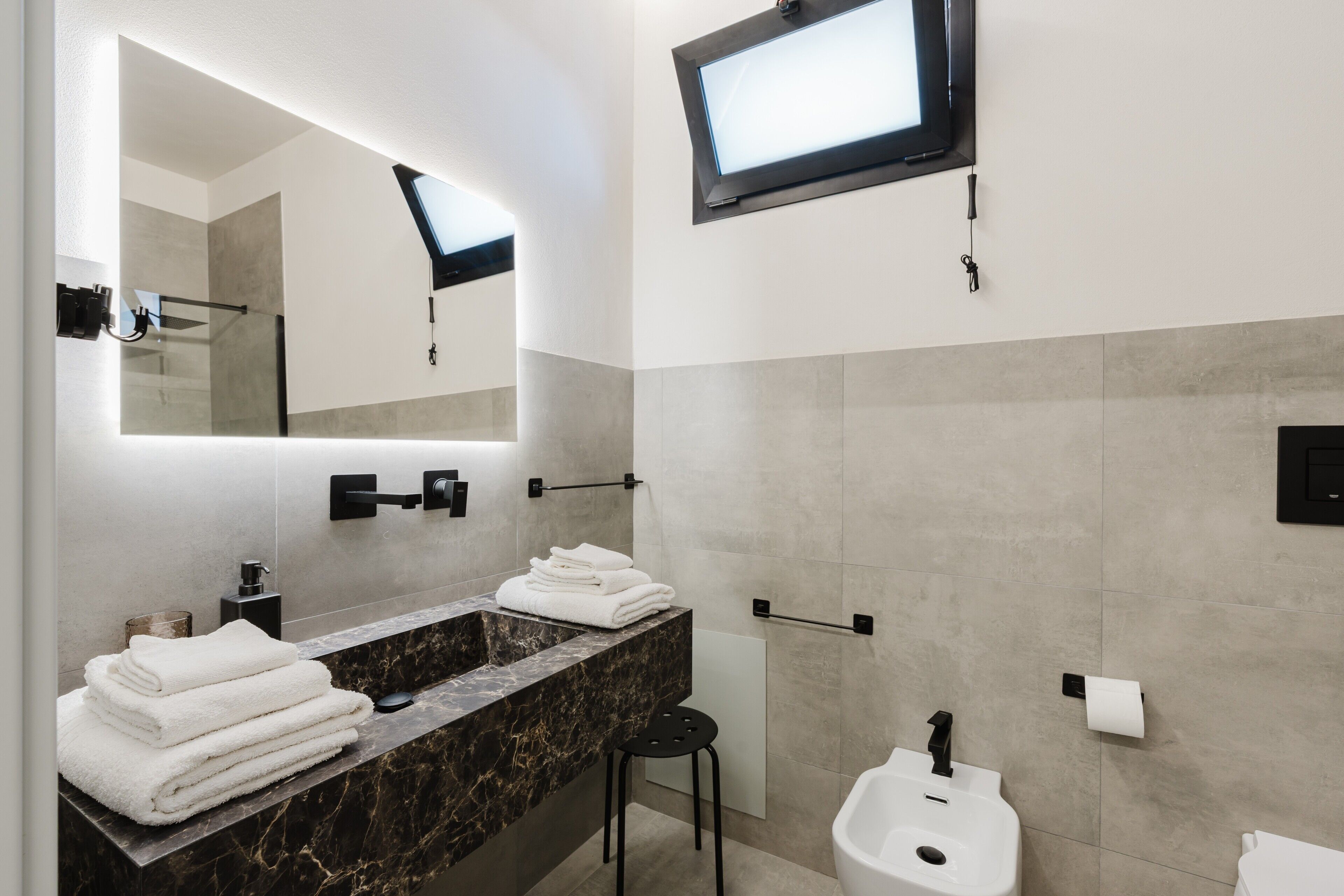 Un bagno moderno con uno specchio grande, un lavandino, un water e una televisione montata a parete.