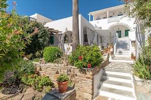 Un bâtiment blanc avec un escalier en pierre menant à une porte verte, entouré de plantes en pot et de verdure.