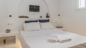 Une chambre d’hôtel minimaliste comprenant un lit, une petite table de chevet, un tableau accroché au mur et une fenêtre.