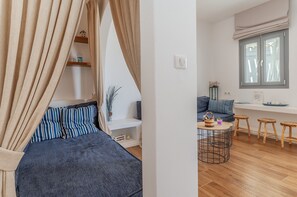 Une chambre à coucher avec un lit, des rideaux, une table de chevet et une étagère ornée d’objets décoratifs.