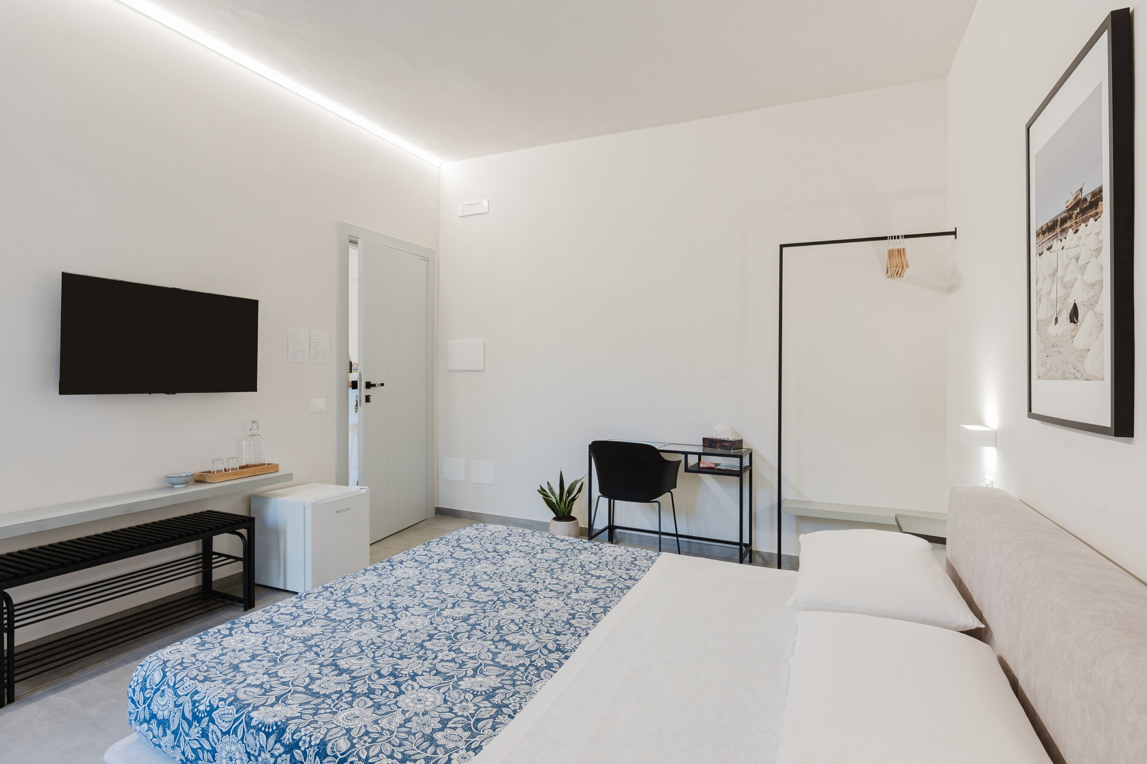 Una camera d'albergo moderna con un letto, una scrivania, una sedia, una TV e una piccola pianta.