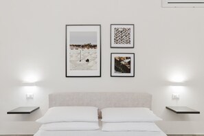 Ein minimalistisch eingerichtetes Hotelzimmer mit einem Bett, zwei Nachttischen und drei gerahmten Bildern an der Wand.