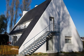 A modern house with a unique triangular roof, a staircase leading to a balcony, and a small window.