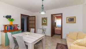 A dining area with a table and chairs, a kitchen with a green cabinet, a sofa, and a door leading to another room.