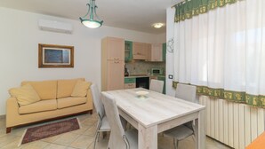 A dining area with a table, chairs, a sofa, and a kitchen in the background.