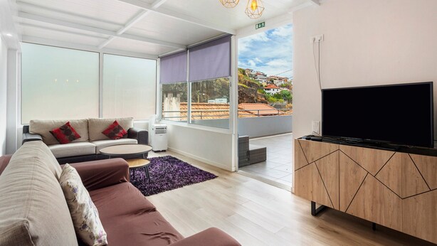 Una sala de estar moderna con un sofá, un televisor de pantalla plana y un amplio ventanal con vistas a una colina.