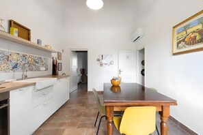 A kitchen with white cabinets, a tiled backsplash, and a wooden dining table with a yellow chair.