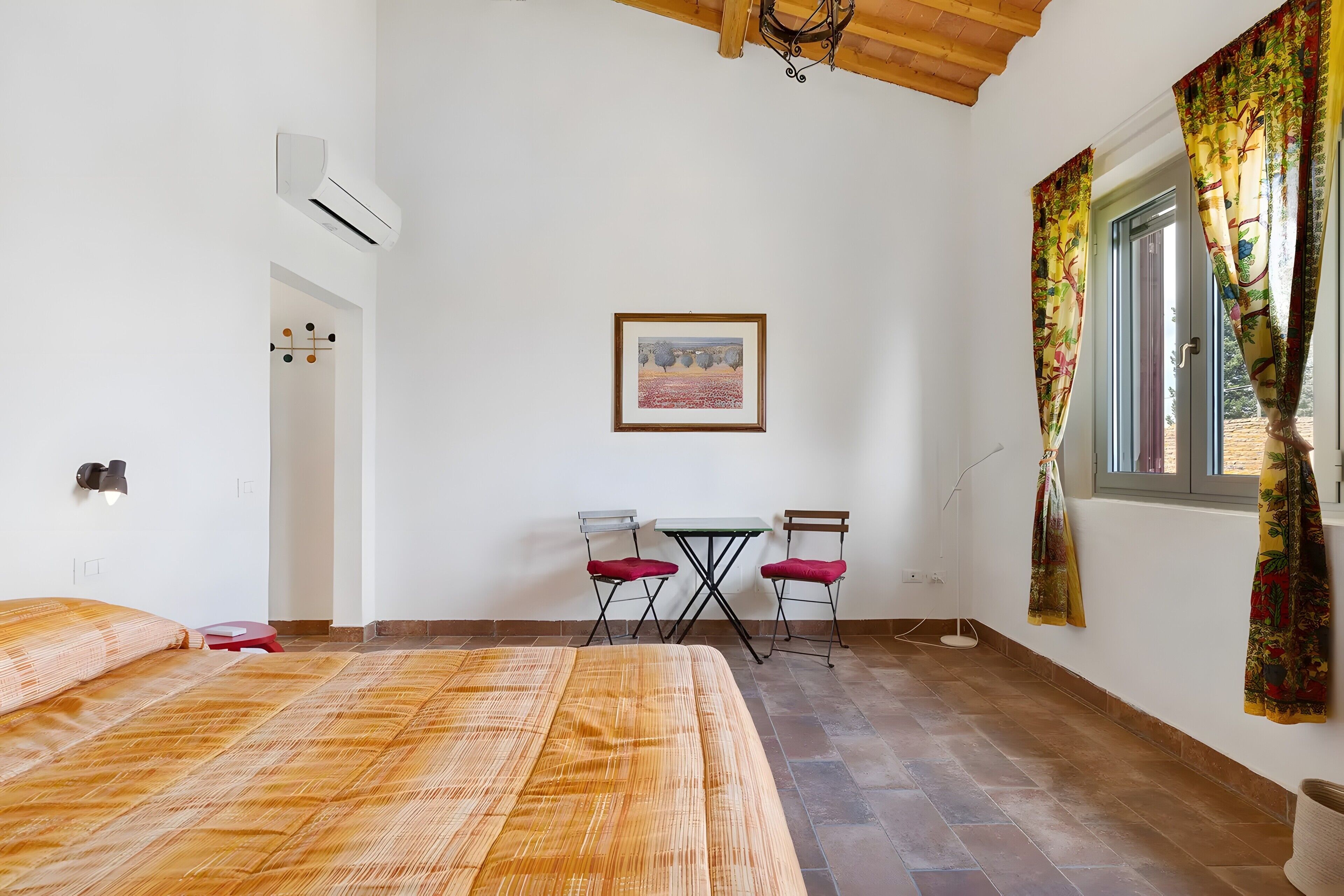 Una habitación con cama, un escritorio con sillas, una ventana con cortinas y un equipo de aire acondicionado.