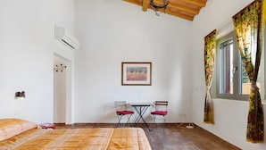 Ein Zimmer mit Bett, Schreibtisch mit Stühlen, einem Fenster mit Vorhängen und einer Klimaanlage.