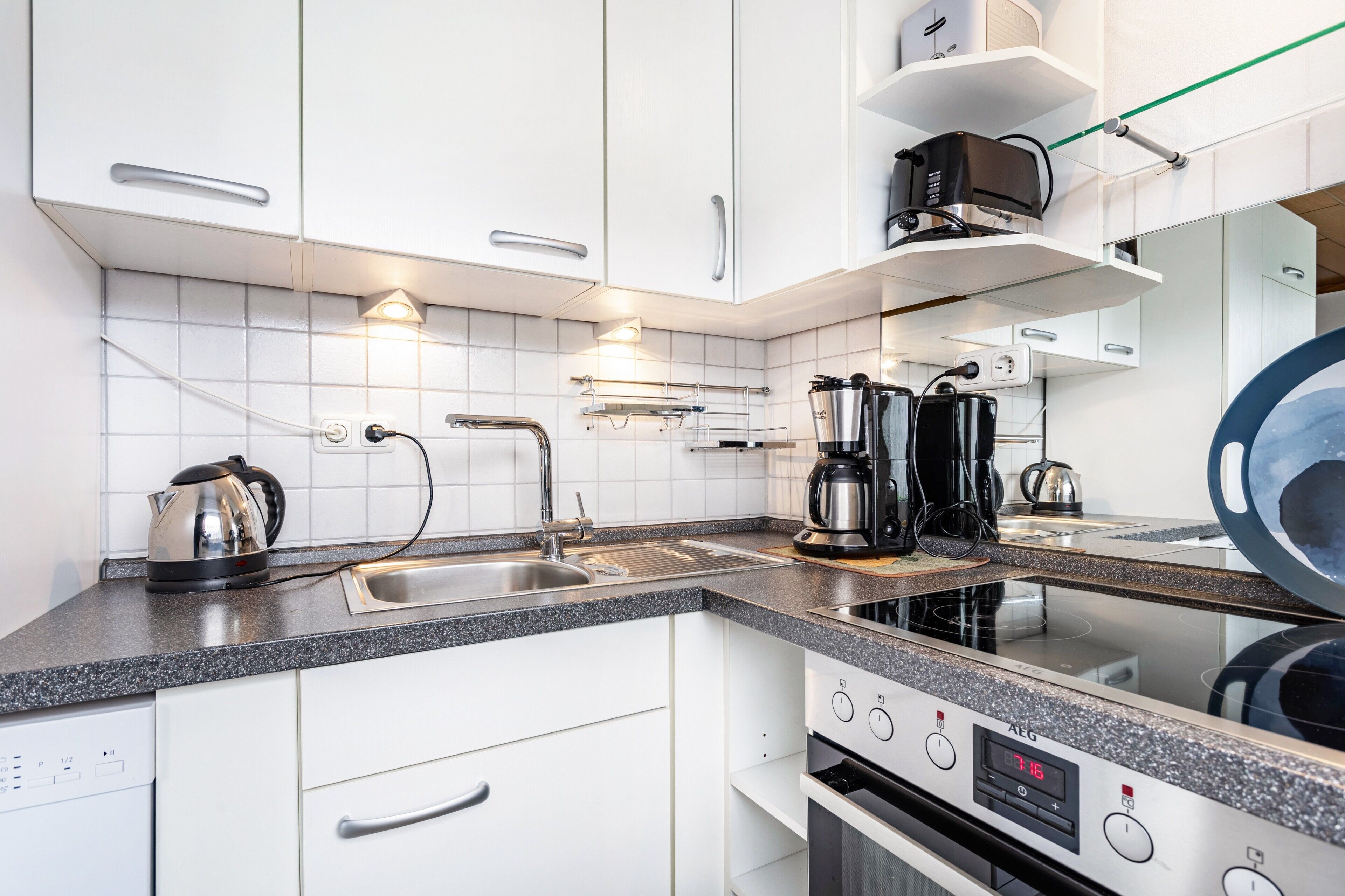 A modern kitchen with white cabinets, a stainless steel kettle, a coffee maker, and an induction cooktop.