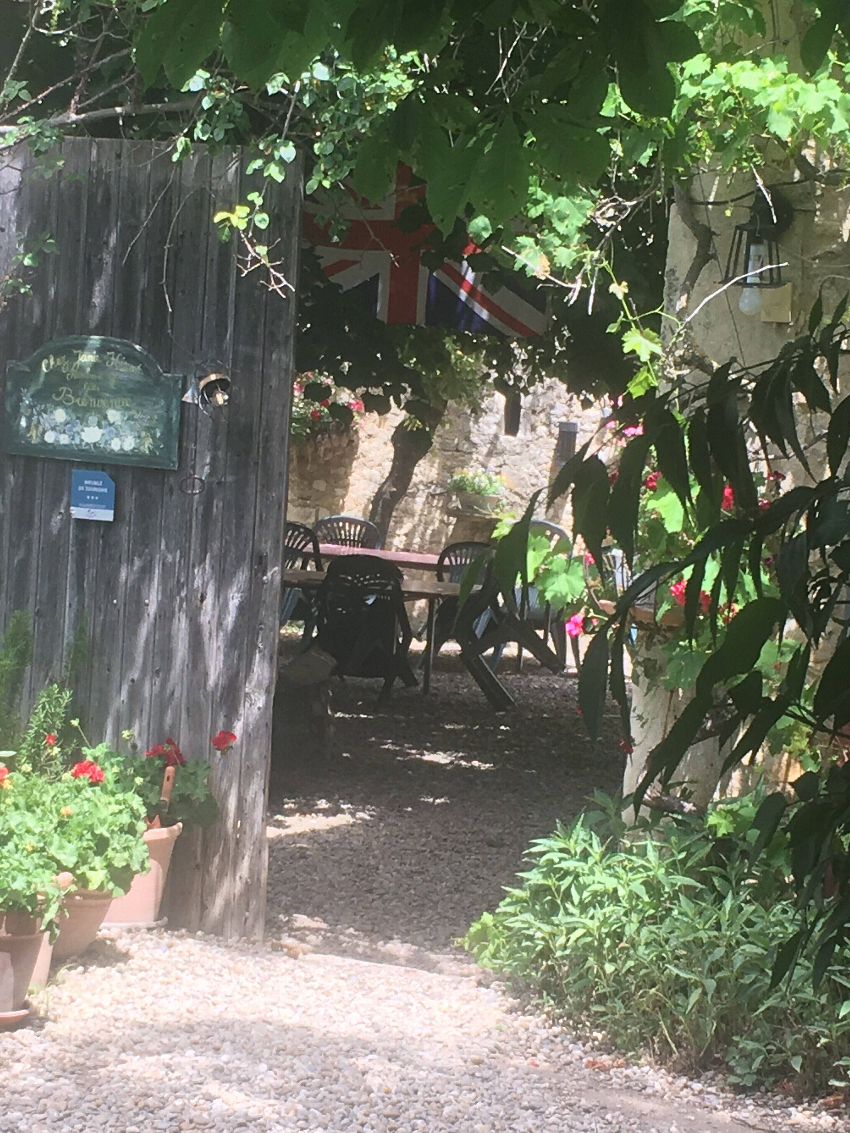Un portón de madera rústico con una placa, un muro de piedra y una bandera.