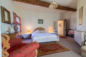 Ein Schlafzimmer mit einem Bett, zwei Nachttischen, einer Holzkommode, einem Stuhl, einem Teppich und einem Heizkörper.