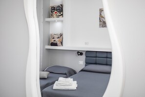 Een moderne slaapkamer met een grijs bed, witte muren en kunstwerken op de planken.