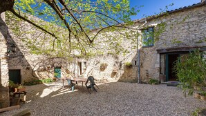 Une cour bordée de murs en pierre, avec un sol recouvert de gravier et une table entourée de chaises.
