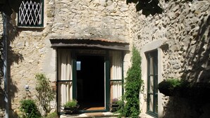 Un bâtiment en pierre doté d’une porte, d’une fenêtre et d’un petit jardin planté.