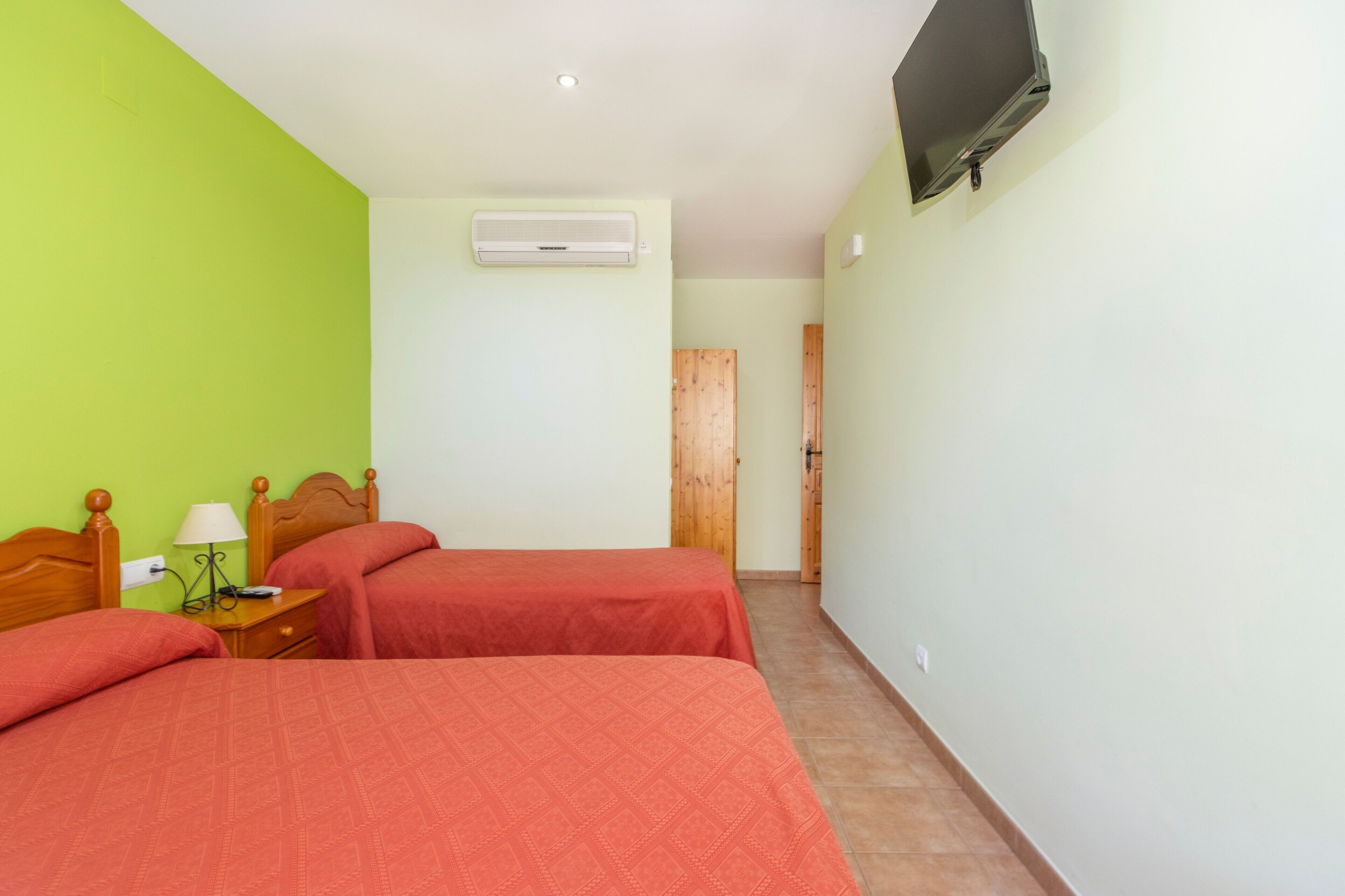 Een kamer met twee bedden, een televisie, een airconditioner en een houten deur.