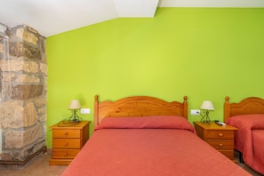 A room with two wooden beds, green walls, a stone wall, and a wooden nightstand with a lamp.