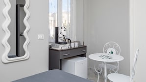 A compact room with a bed, a small desk with a coffee machine, a refrigerator, a white chair, and a mirror. - Room 'Dolce Relax - Deluxe' with Balcony, Wi-Fi and Air Conditioning (Catania)