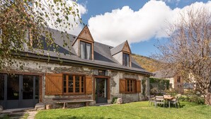 A stone house with wooden shutters, a front door, and a small outdoor seating area.