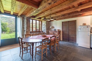 Una cucina rustica con parete in pietra, travi in legno a soffitto, un tavolo da pranzo con sedie e un frigorifero.