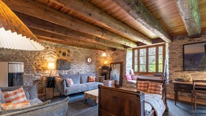A rustic interior with stone walls, wooden beams, a bed, a sofa, and a dining area.