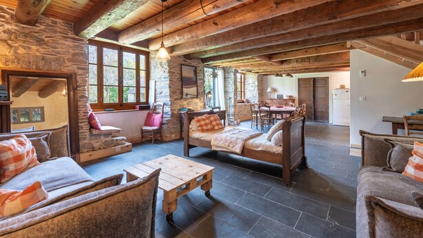A rustic interior with stone walls, wooden beams, a stone fireplace, and a dining area.