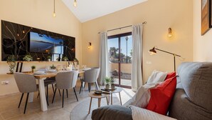 Un salon moderne doté d’un téléviseur à écran plat, d’un coin repas et d’une grande fenêtre agrémentée de rideaux.