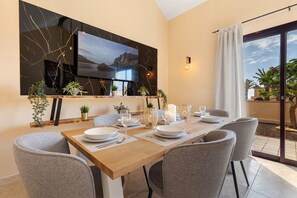 A dining area with a wooden table set for four, a flat-screen TV mounted on the wall, and potted plants on the windowsill.