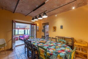 Un coin repas avec une table dressée pour quatre personnes, entourée de chaises, une fenêtre donnant sur un beau paysage et un plafond en briques.