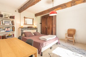 Une chambre à coucher avec un lit, des poutres en bois, une bibliothèque, une chaise et une table.