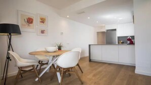A modern kitchen with white cabinets, a wooden dining table, and white chairs. - Spectacular Penthouse with Sagrada Familia Views (Barcelona)