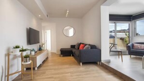 A modern living room with a sofa, a coffee table, and a TV mounted on the wall. There is a round mirror on the wall and a small table with plants. - Spectacular Penthouse with Sagrada Familia Views (Barcelona)