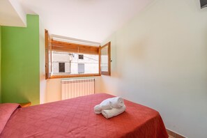 A bedroom with a bed, a window with blinds, a radiator, and a green wall.