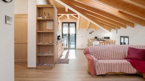 A cozy room with a wooden ceiling, a sofa, a bookshelf, and a kitchen area. - Holiday Home 'Sam Fiamet' with Mountain View, Shared Garden and Wi-Fi (GROSIO)