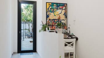 Un corridoio con una porta che dà su un'area esterna, una reception bianca e un quadro astratto dai colori vivaci appeso al muro.