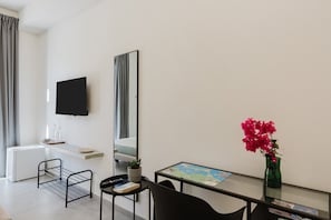 Et moderne værelse med seng, fjernsyn, skrivebord med et kort, en plante og et spejl.